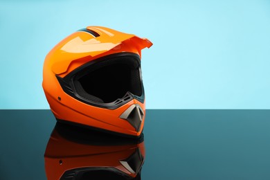 Modern motorcycle helmet with visor on mirror surface against light blue background. Space for text