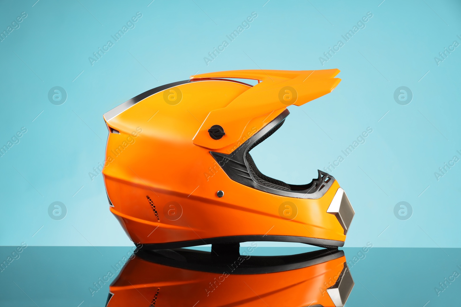 Photo of Modern motorcycle helmet with visor on mirror surface against light blue background