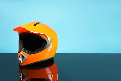 Modern motorcycle helmet with visor on mirror surface against light blue background. Space for text