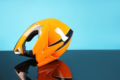 Photo of Modern motorcycle helmet with visor on mirror surface against light blue background. Space for text