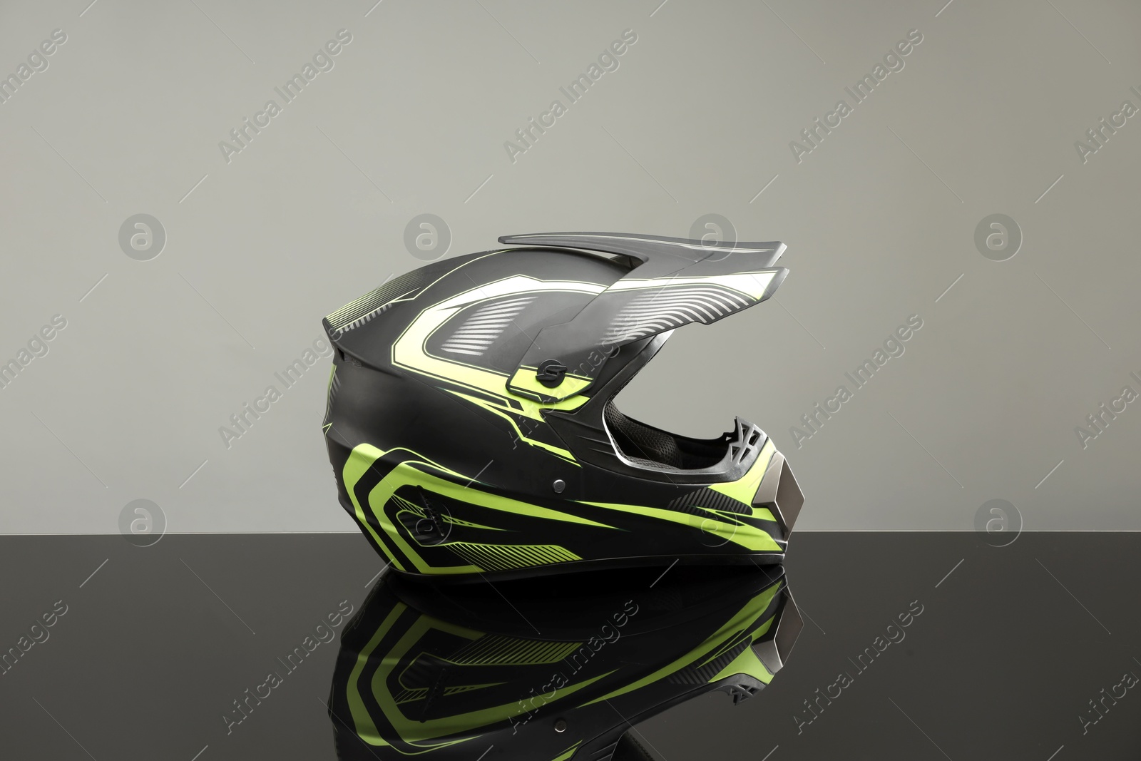 Photo of Modern motorcycle helmet with visor on mirror surface against light grey background