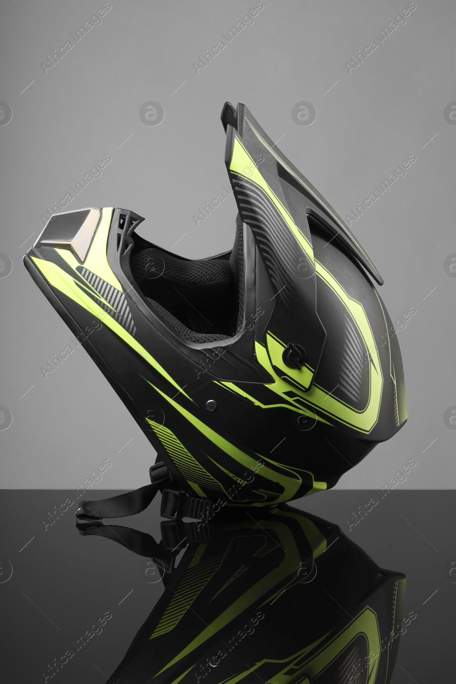 Photo of Modern motorcycle helmet with visor on mirror surface against light grey background