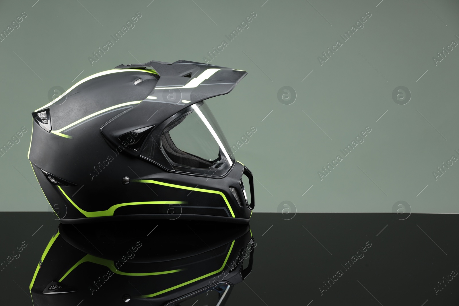 Photo of Modern motorcycle helmet with visor on mirror surface against light grey background. Space for text