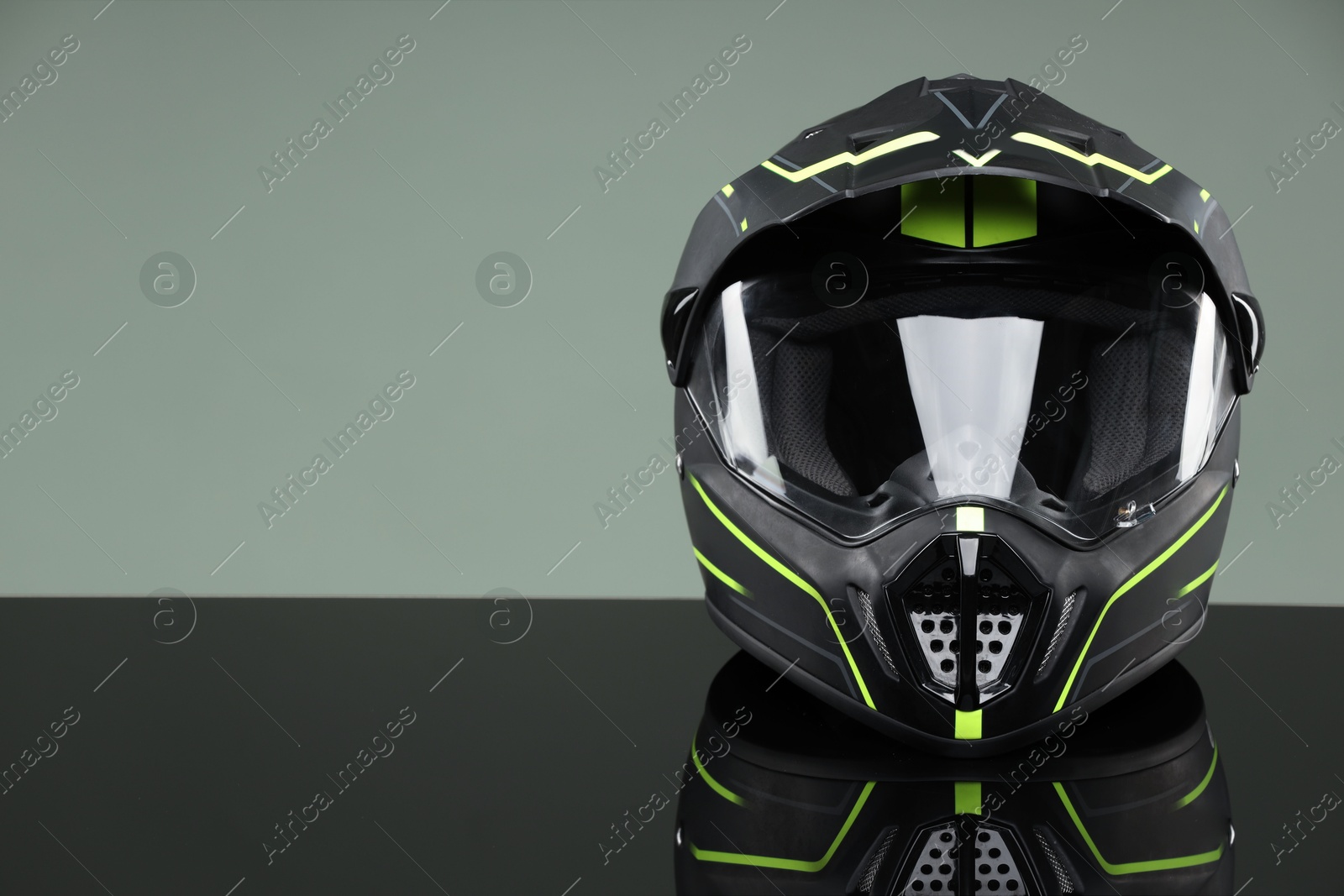 Photo of Modern motorcycle helmet with visor on mirror surface against light grey background. Space for text