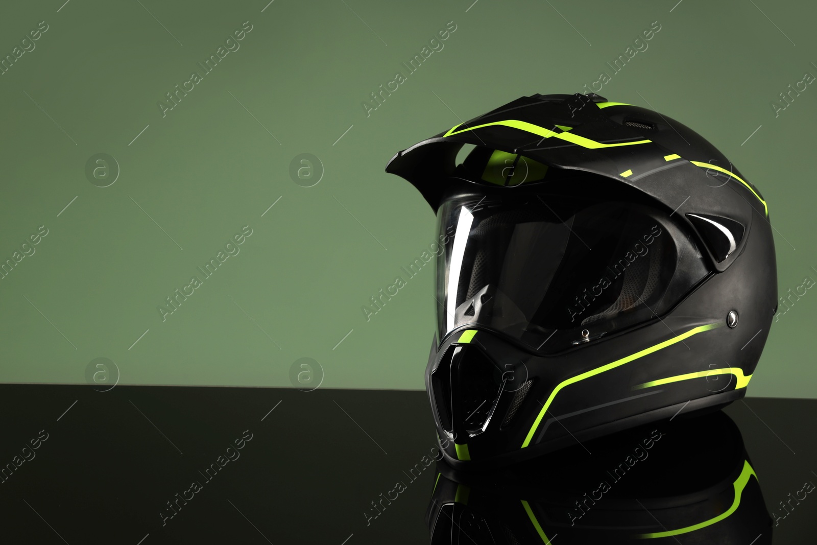 Photo of Modern motorcycle helmet with visor on mirror surface against light green background. Space for text