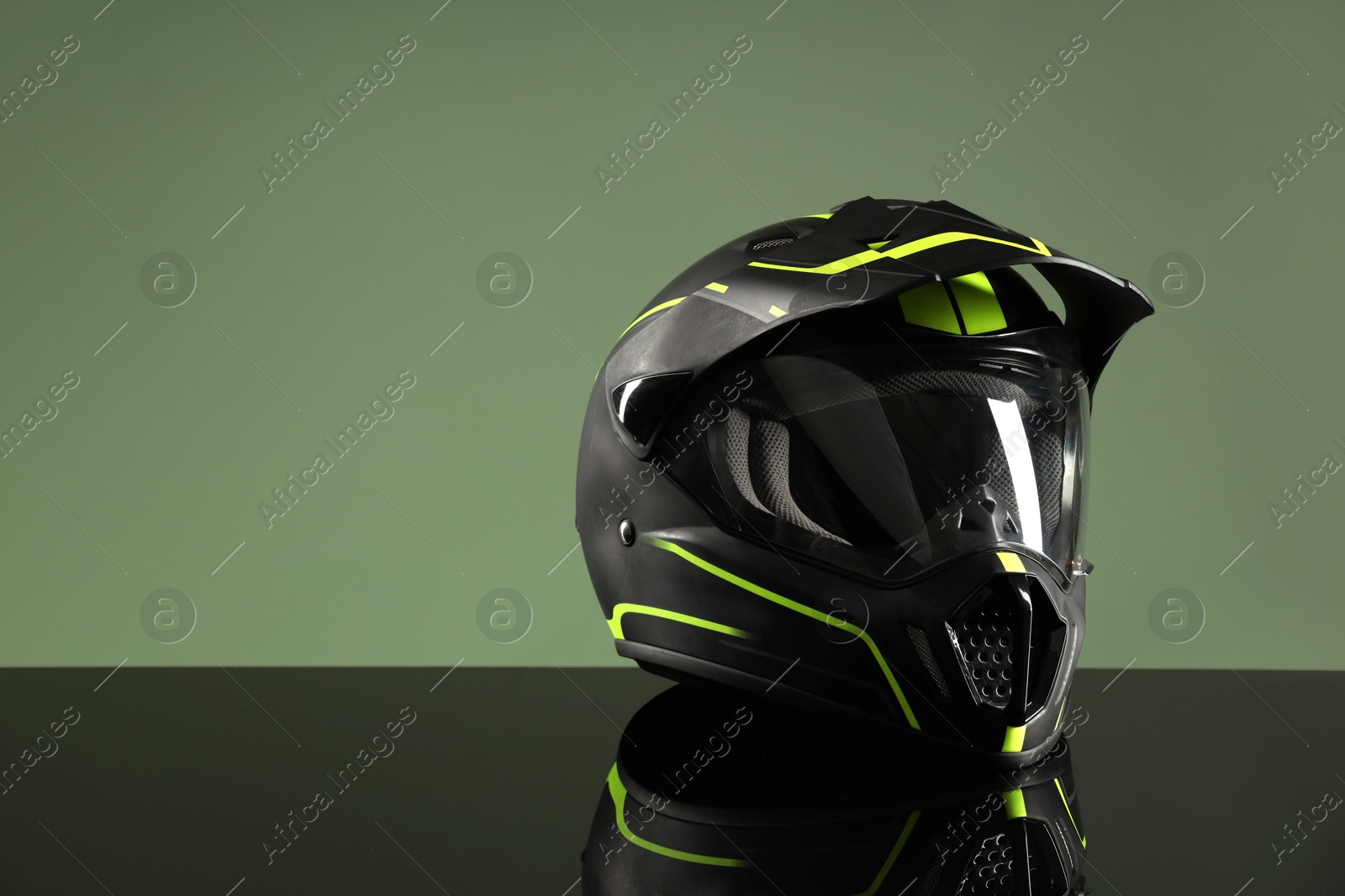 Photo of Modern motorcycle helmet with visor on mirror surface against light green background. Space for text