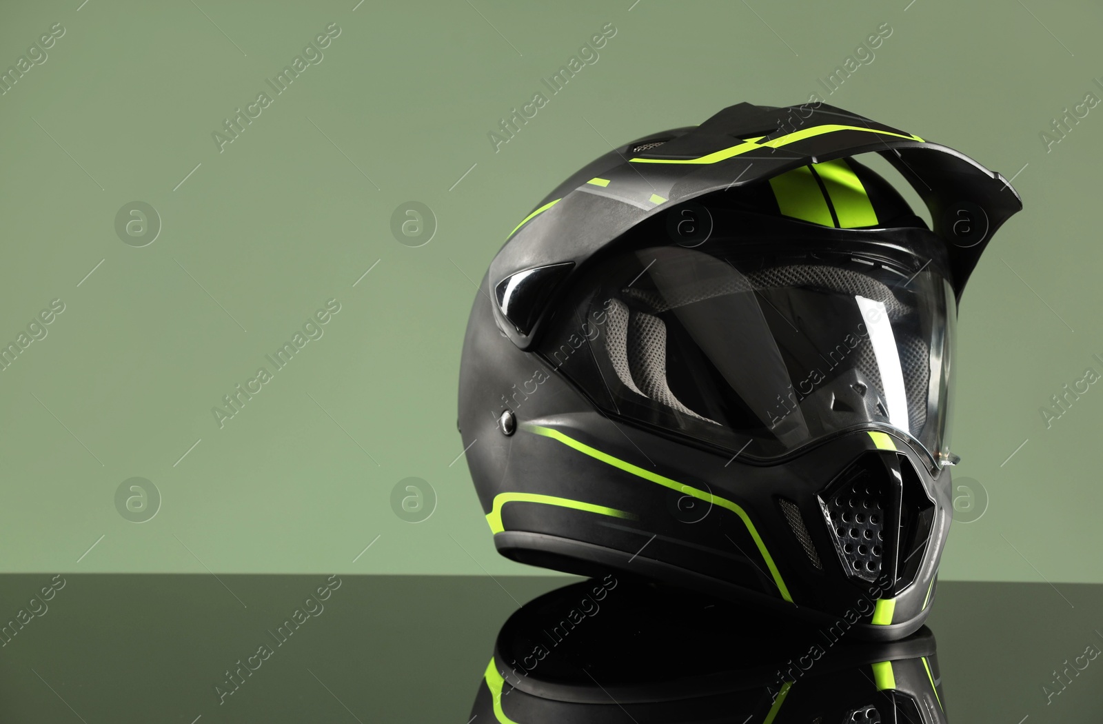 Photo of Modern motorcycle helmet with visor on mirror surface against light green background. Space for text