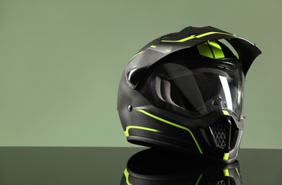 Photo of Modern motorcycle helmet with visor on mirror surface against light green background. Space for text