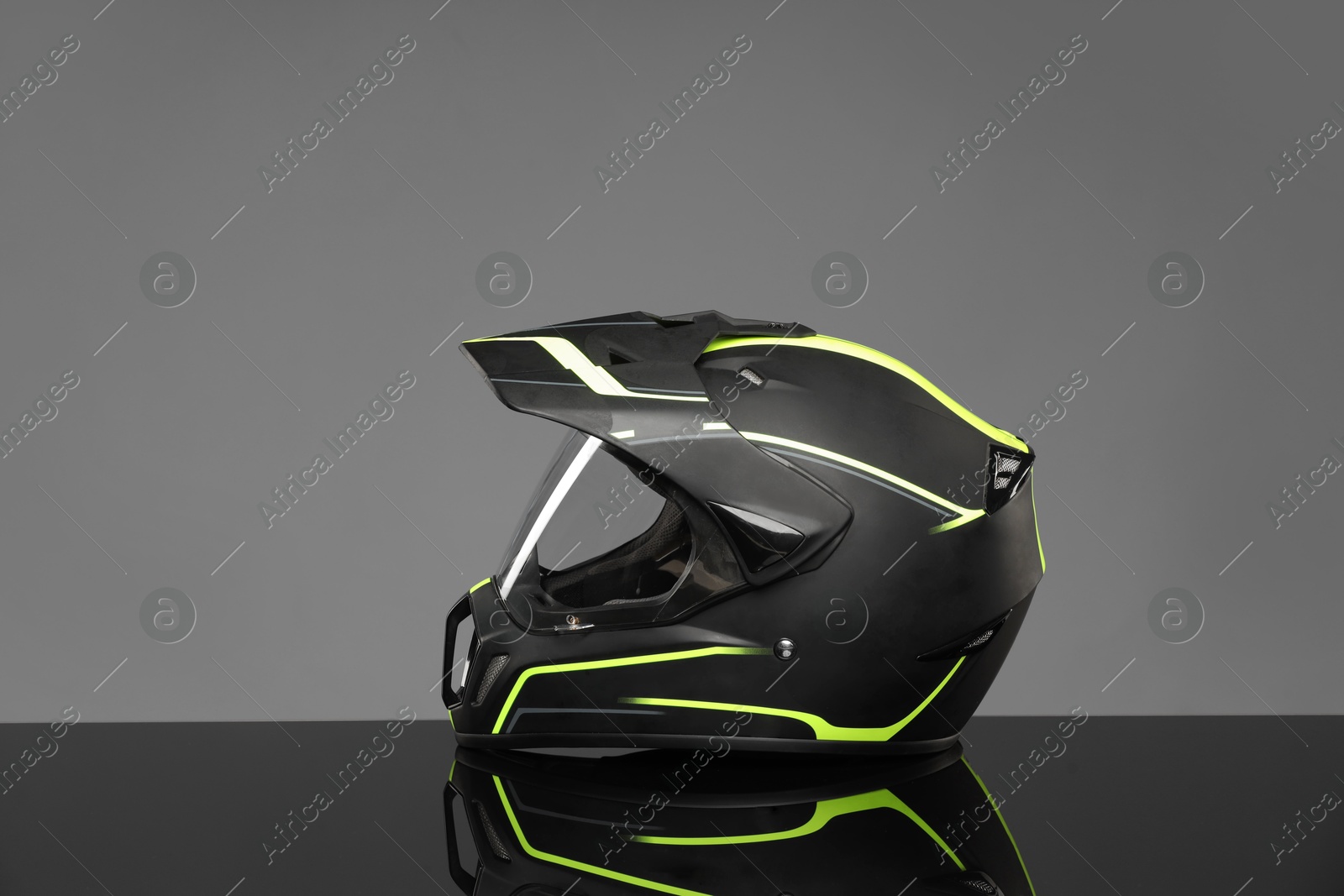 Photo of Modern motorcycle helmet with visor on mirror surface against light grey background. Space for text