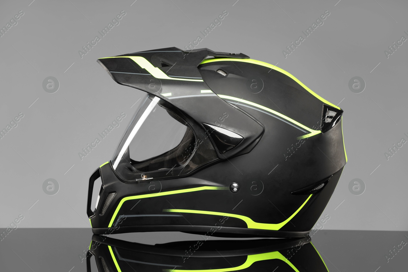 Photo of Modern motorcycle helmet with visor on mirror surface against light grey background