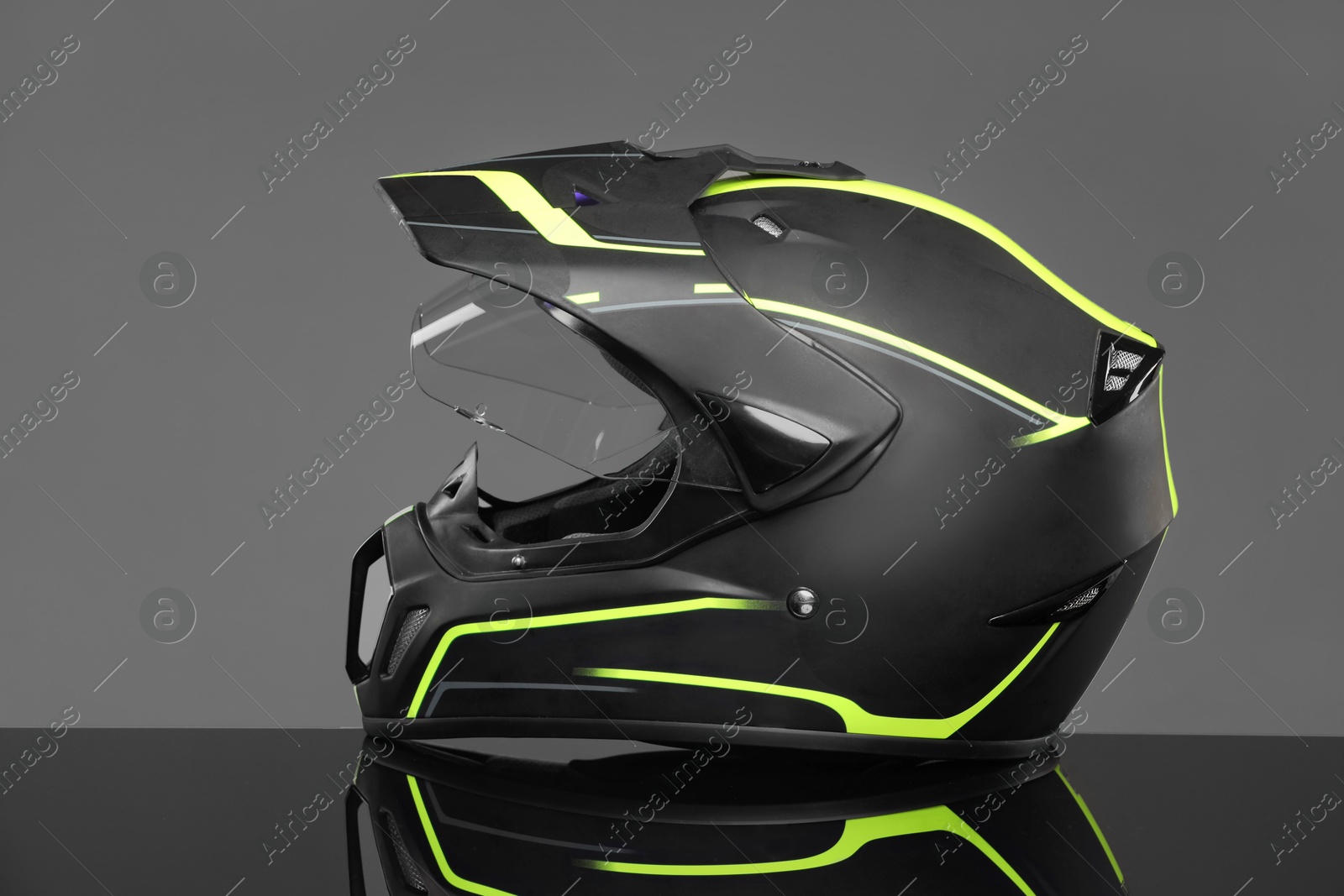 Photo of Modern motorcycle helmet with visor on mirror surface against light grey background