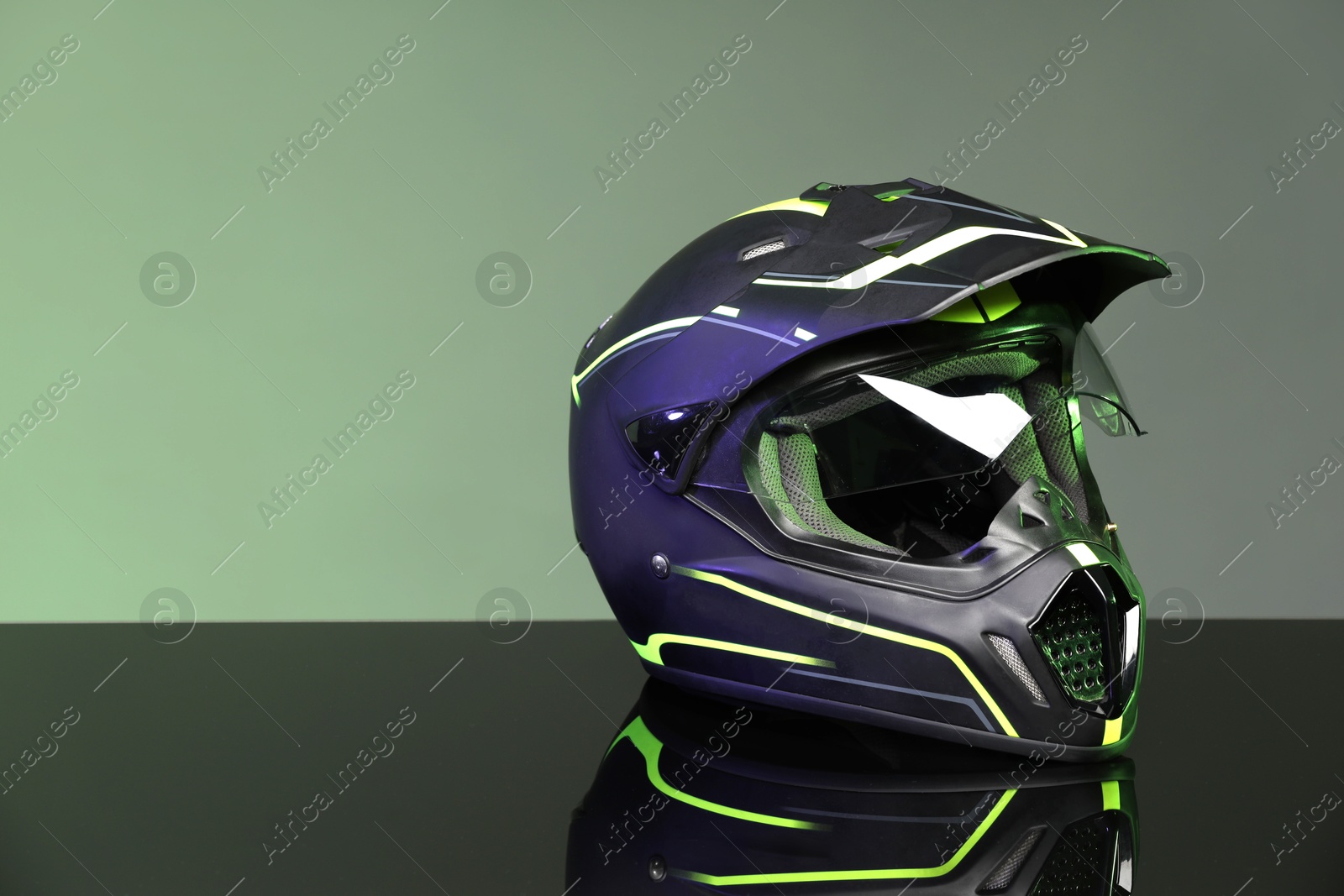 Photo of Modern motorcycle helmet with visor on mirror surface against grey background. Space for text