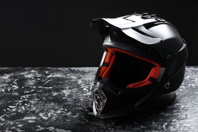 Modern motorcycle helmet with visor on grey stone surface against black background. Space for text