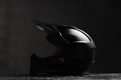Photo of Modern motorcycle helmet with visor on grey stone surface against black background