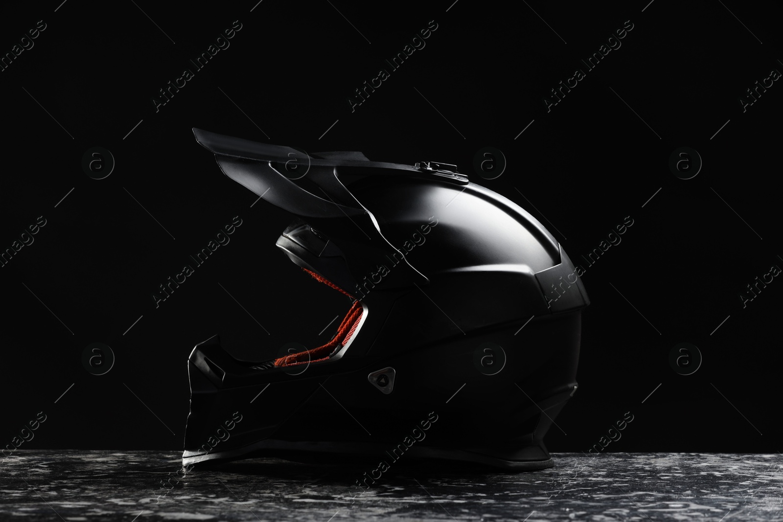 Photo of Modern motorcycle helmet with visor on grey stone surface against black background