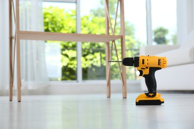 Photo of Cordless electric screwdriver on floor at home. Space for text