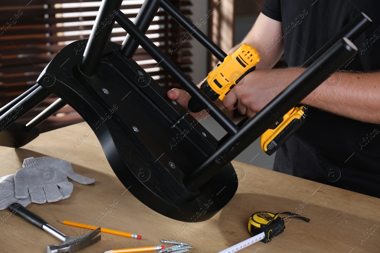 Photo of Man with electric screwdriver assembling chair in room, closeup