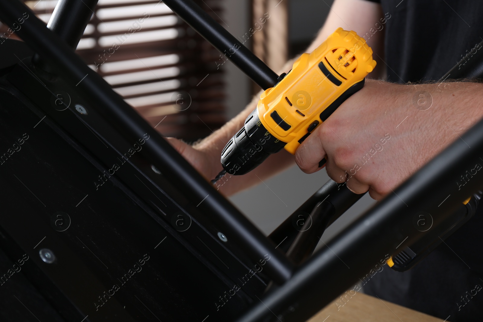 Photo of Man with electric screwdriver assembling furniture in room, closeup