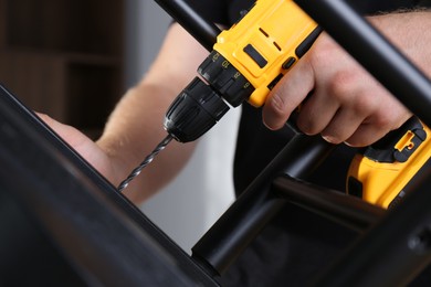 Man with electric screwdriver assembling furniture in room, closeup