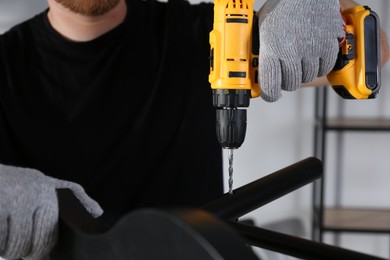 Man with electric screwdriver assembling chair in room, closeup