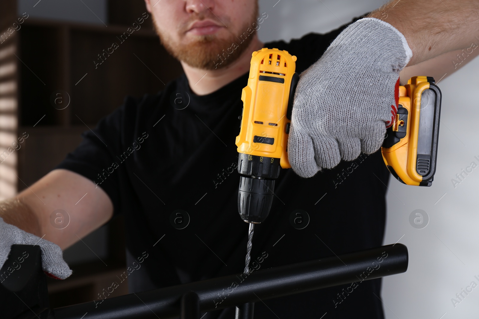 Photo of Man with electric screwdriver assembling furniture indoors, closeup