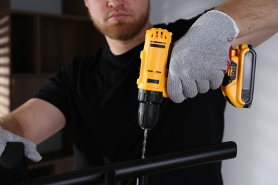 Photo of Man with electric screwdriver assembling furniture indoors, closeup