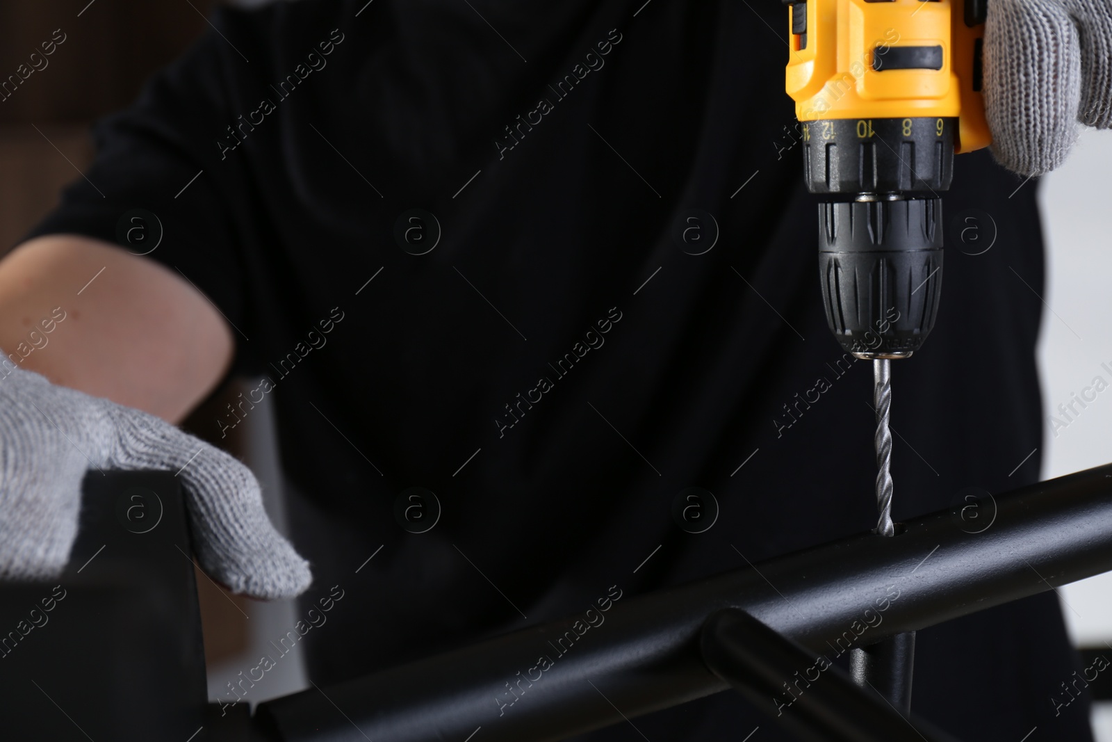 Photo of Man with electric screwdriver assembling furniture indoors, closeup