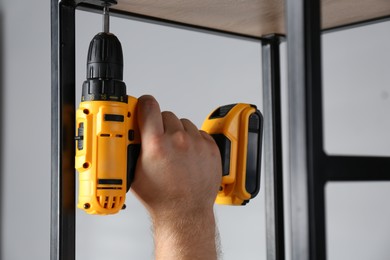 Photo of Man with electric screwdriver assembling furniture indoors, closeup