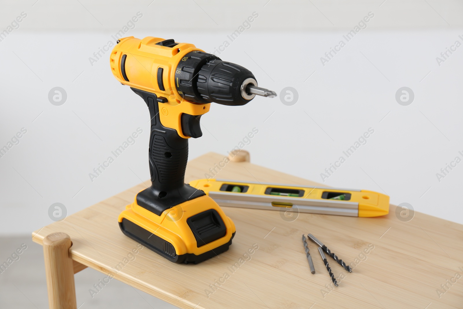 Photo of Electric screwdriver, drill bits and building level on wooden table against light background