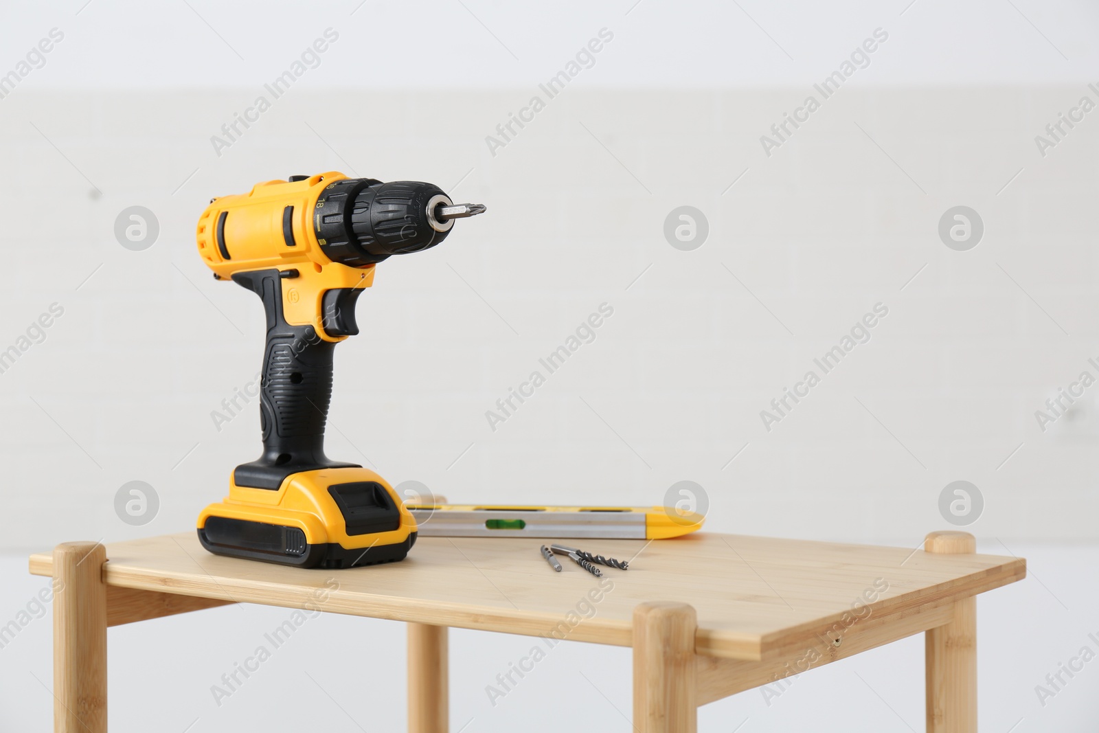 Photo of Electric screwdriver, drill bits and building level on wooden table against light background. Space for text