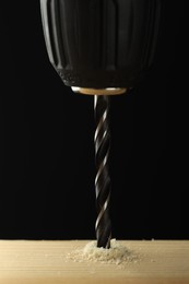 Photo of Drilling hole in wooden plank on black background, closeup