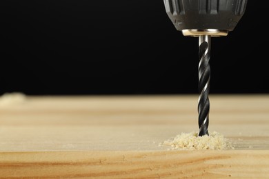 Photo of Drilling hole in wooden plank on black background, closeup. Space for text