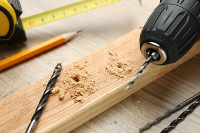 Photo of Cordless electric drill, bits and holed plank on wooden table, closeup