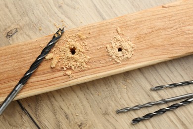 Photo of Plank with holes, drill bits and sawdust on wooden table, flat lay