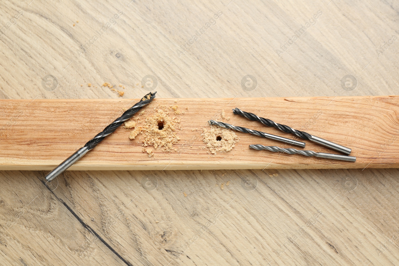 Photo of Plank with holes, drill bits and sawdust on wooden table, flat lay