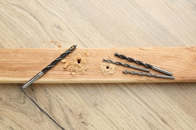 Plank with holes, drill bits and sawdust on wooden table, flat lay