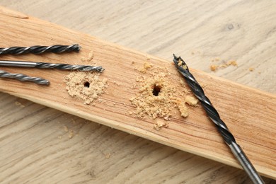 Plank with holes, drill bits and sawdust on wooden table, flat lay