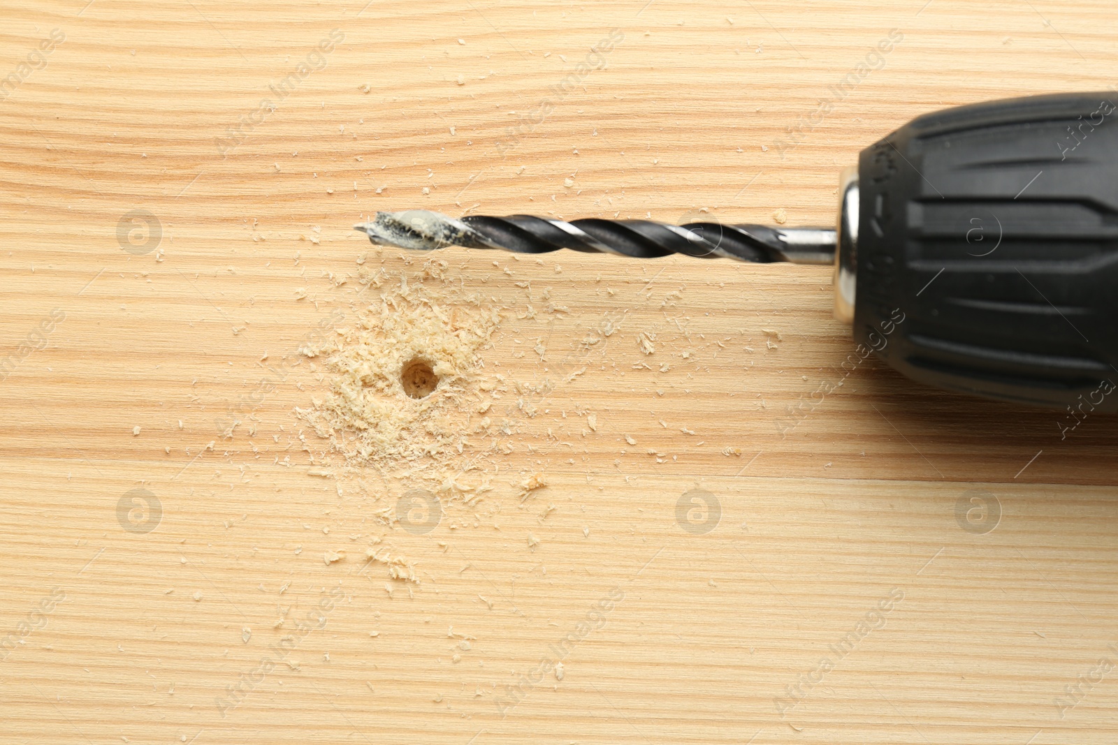 Photo of Cordless electric drill on holed wooden surface, top view