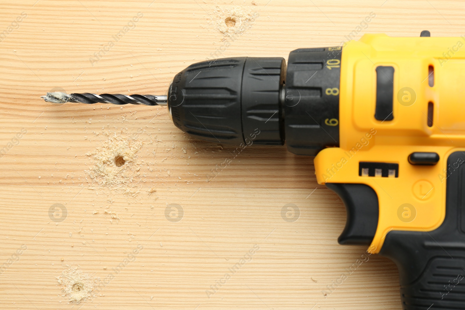 Photo of Cordless electric drill on holed wooden surface, top view