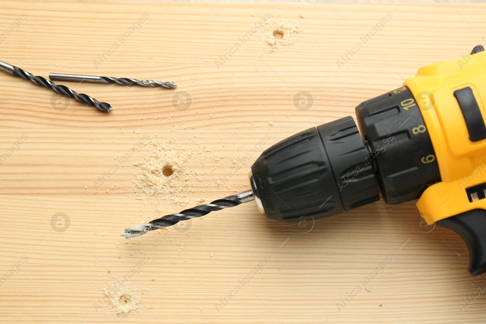 Photo of Cordless electric drill and bits on holed wooden surface, flat lay