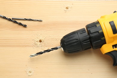 Cordless electric drill and bits on holed wooden surface, flat lay