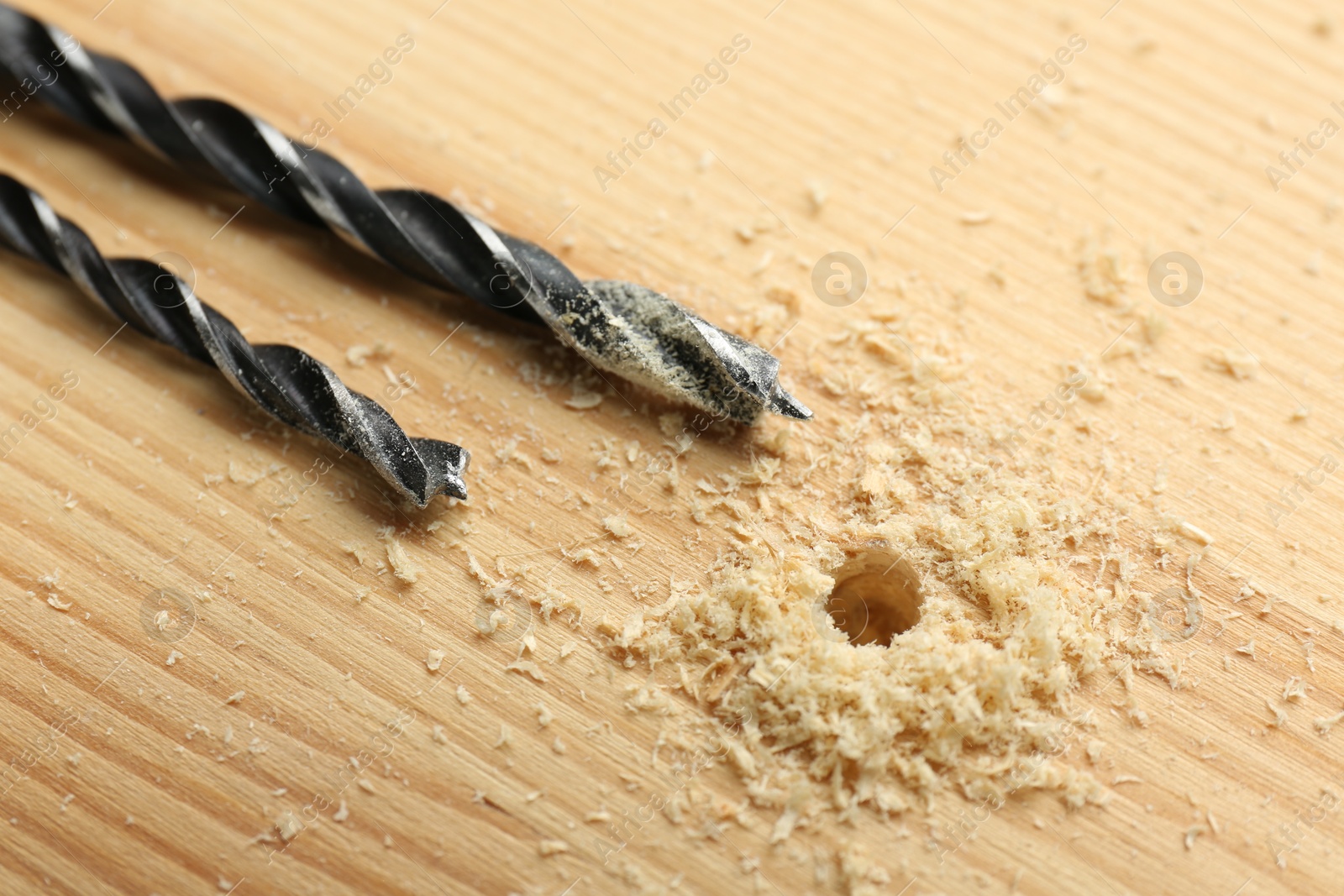 Photo of Drill bits and sawdust on holed wooden surface, closeup