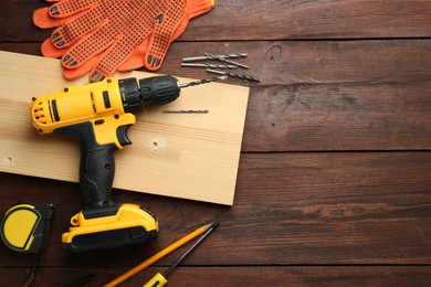 Photo of Cordless electric drill, gloves, plank and construction tools on wooden table, flat lay. Space for text