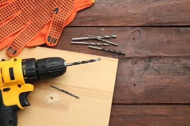 Photo of Cordless electric drill, gloves, bits and plank on wooden table, flat lay. Space for text