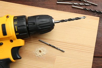 Cordless electric drill, bits and holed plank on wooden table