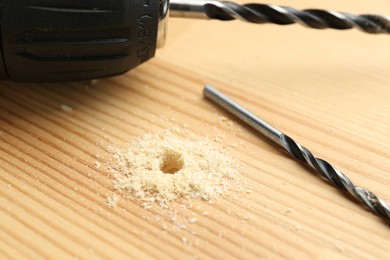 Cordless electric drill and bit on holed wooden surface, closeup