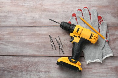 Cordless electric drill, gloves and bits on wooden table, flat lay. Space for text