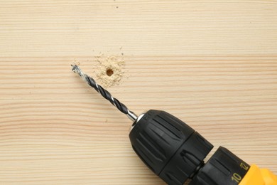 Photo of Cordless electric drill on holed wooden surface, top view