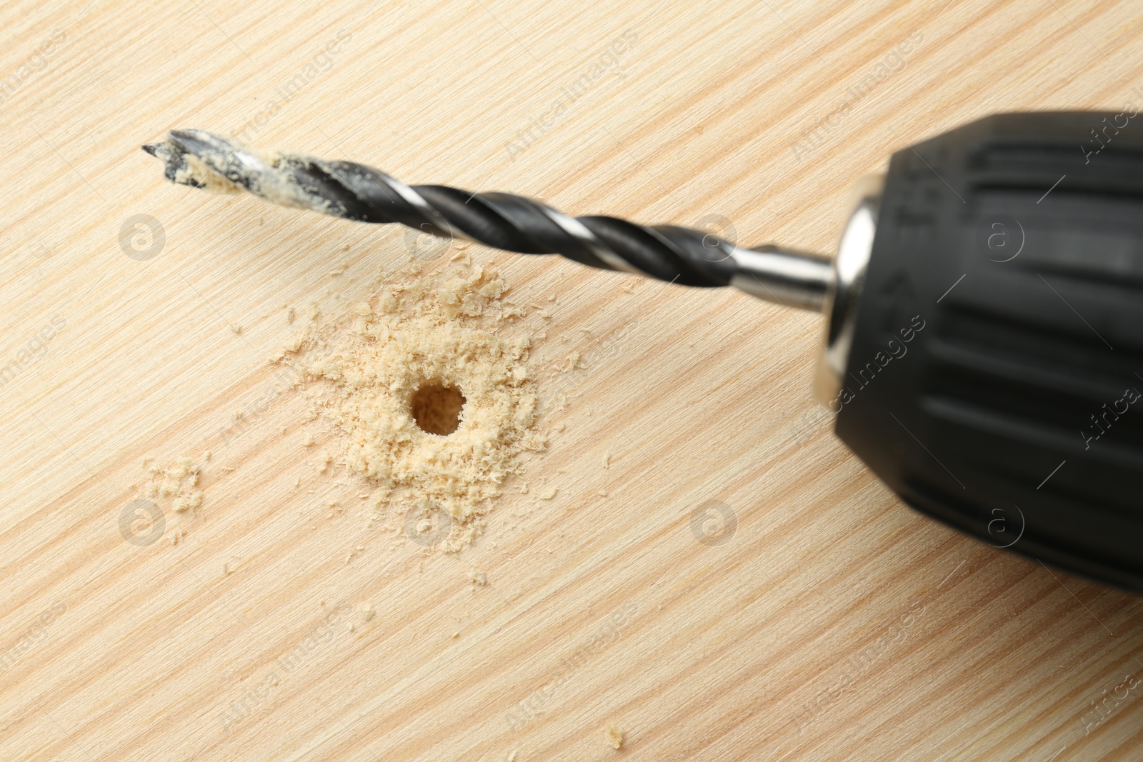 Photo of Cordless electric drill on holed wooden surface, top view