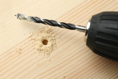 Photo of Cordless electric drill on holed wooden surface, top view